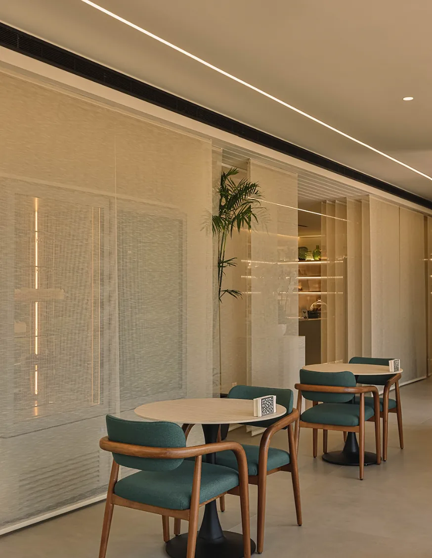 Muscador café interior with sage-green chairs and woven glass partitions